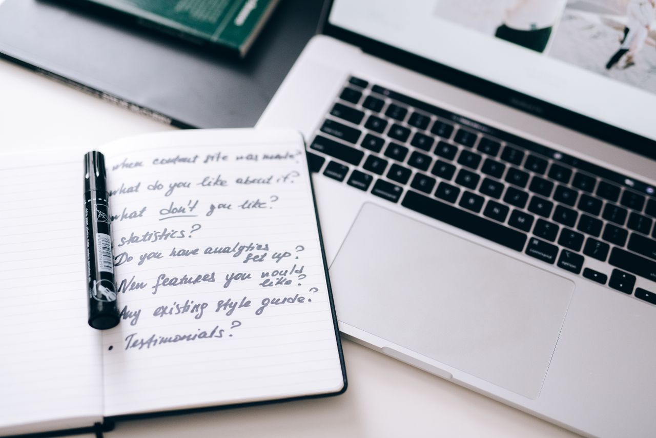 Home A notebook with handwritten notes next to a laptop on a workspace desk.