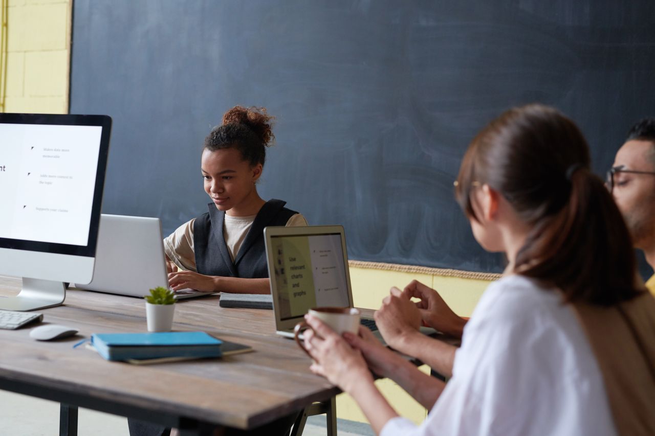 creative Group of young adults engaged in digital learning with laptops and desktops in a contemporary classroom.