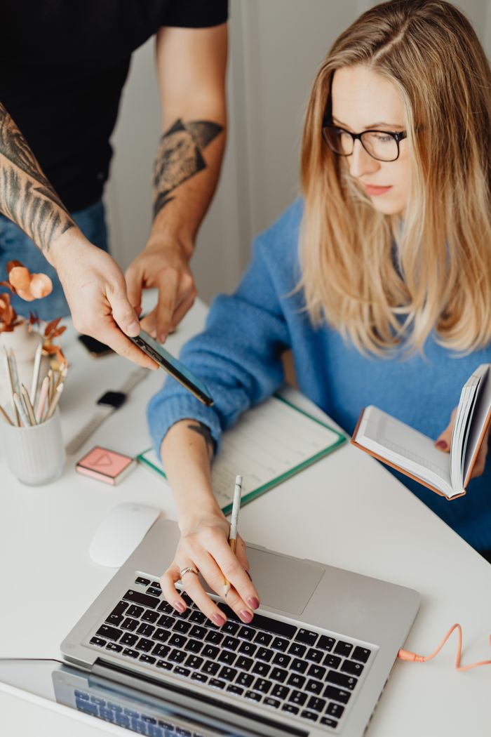 Woman in blue sweater working on a laptop at home office desk.