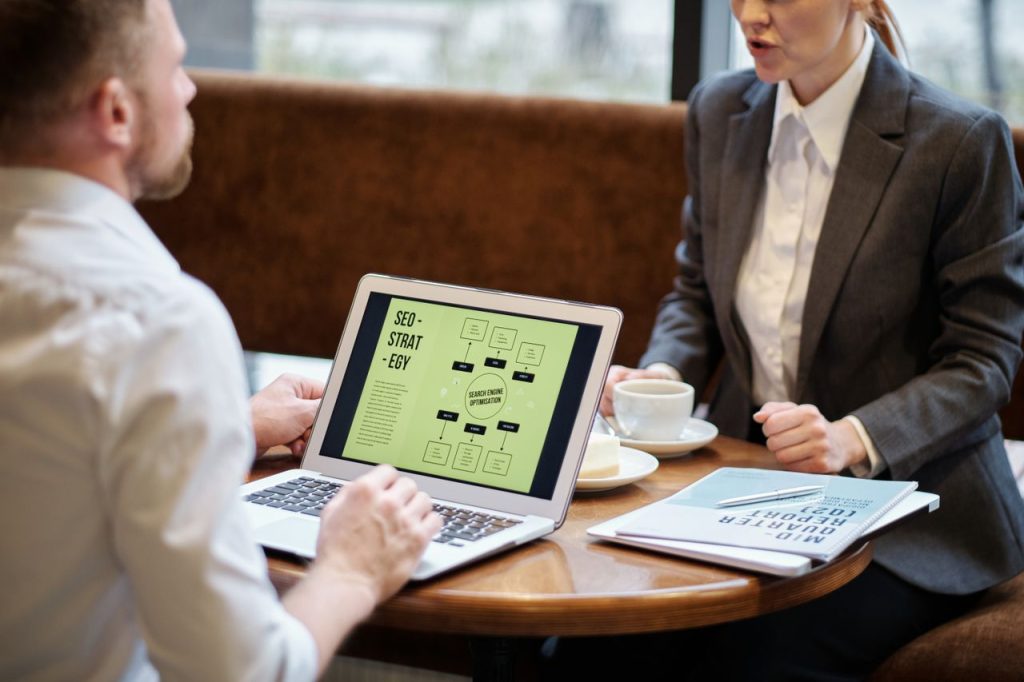 A man and woman engaged in a business meeting discussing SEO strategy in a cozy cafe setting.